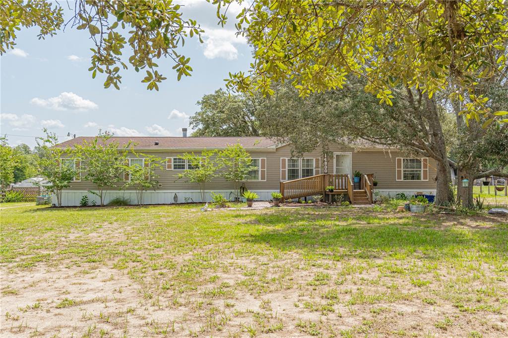 A single-story manufactured home with tan siding, a wooden ramp, and a large front yard — 14800 HAYS ROAD, SPRING HILL, FL