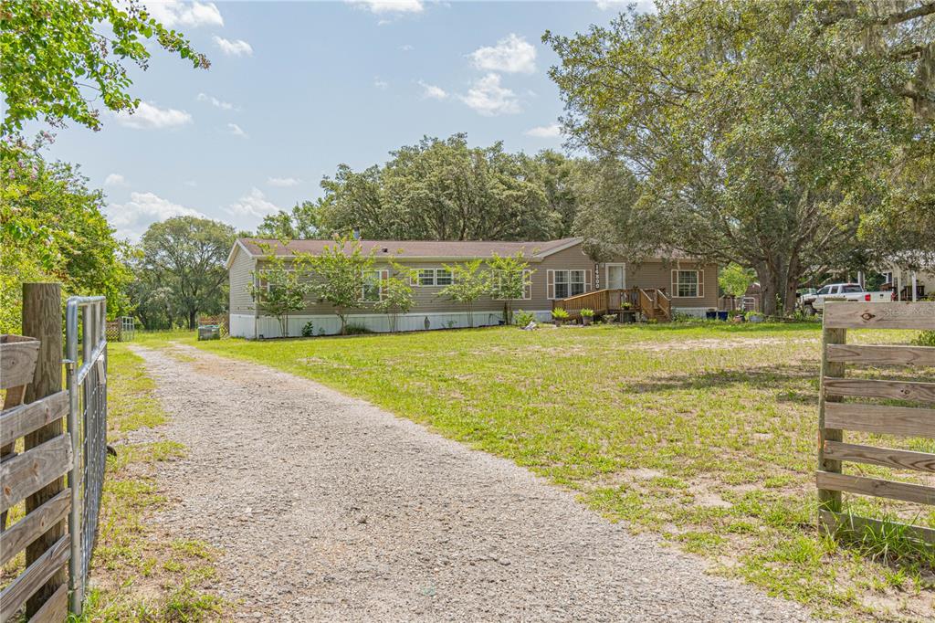 A gravel driveway leads to a single-story manufactured home surrounded by trees and grass — 14800 HAYS ROAD, SPRING HILL, FL
