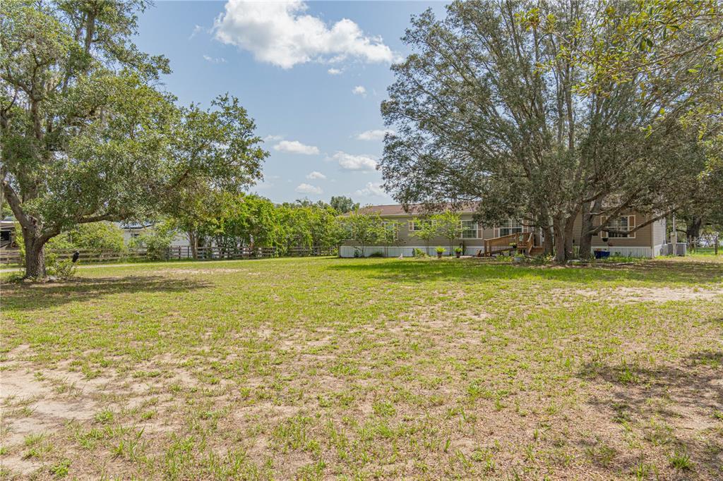 A single-story manufactured home sits on a large, grassy lot shaded by mature trees — 14800 HAYS ROAD, SPRING HILL, FL