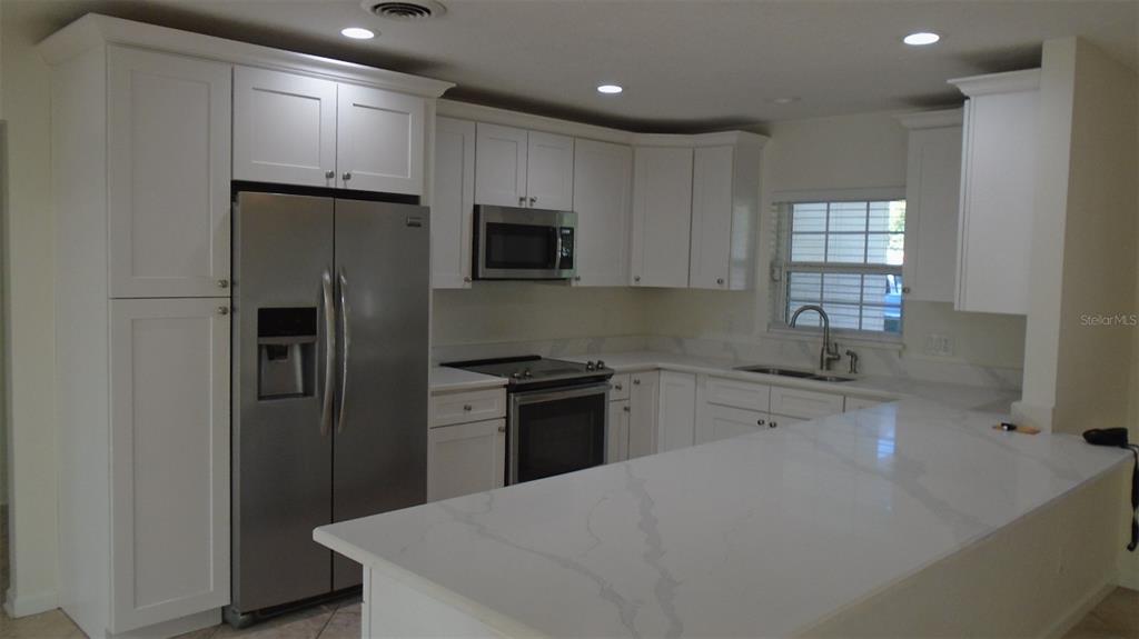 A kitchen features white cabinets, stainless steel appliances, and a white quartz-topped island — 420 ARAPAHO TRAIL, MAITLAND, FL