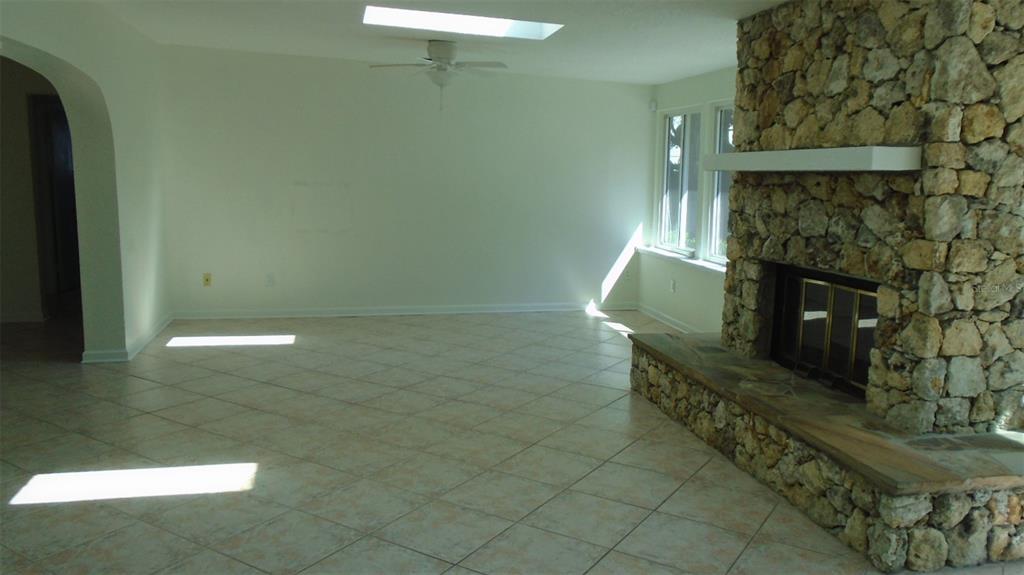 A living room features a stone fireplace, tile flooring, a ceiling fan, and a skylight — 420 ARAPAHO TRAIL, MAITLAND, FL