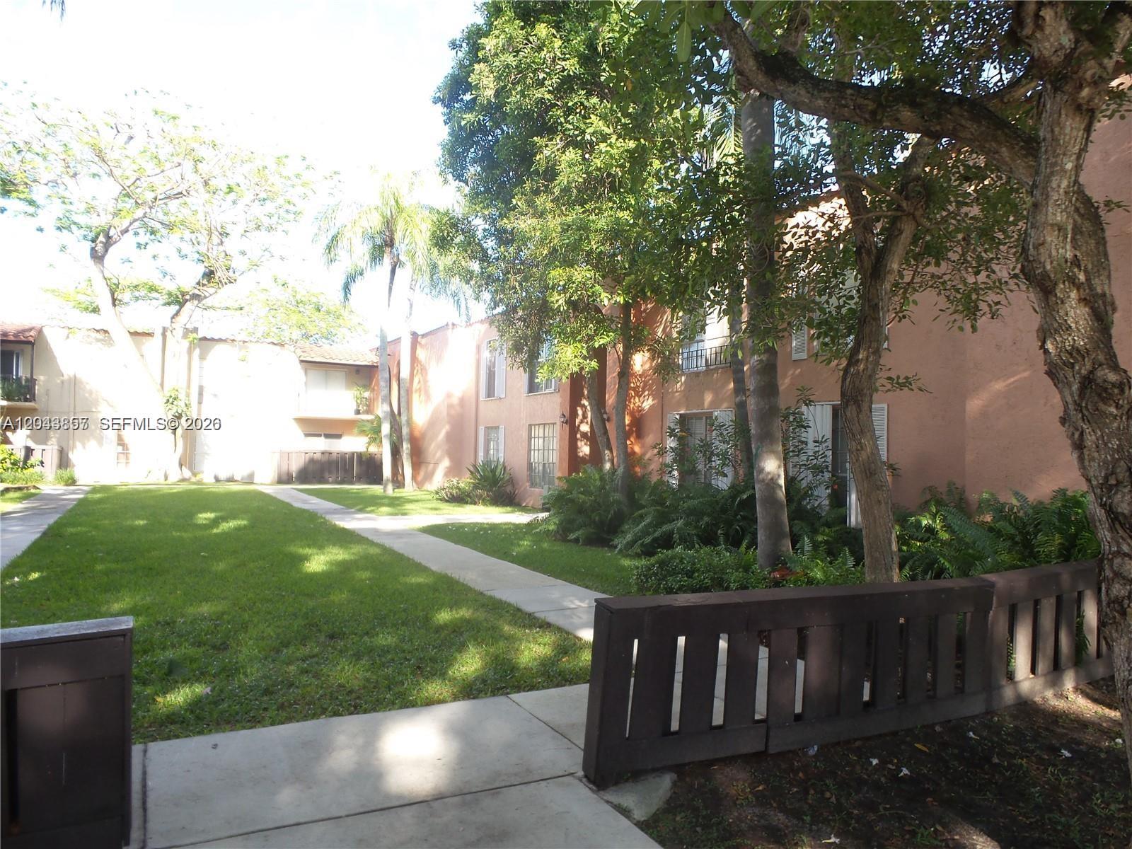 A grassy courtyard sits between two-story stucco apartment buildings with walkways and mature trees — 10794 N Kendall Dr # B22, Miami FL 33176, MIAMI, FL