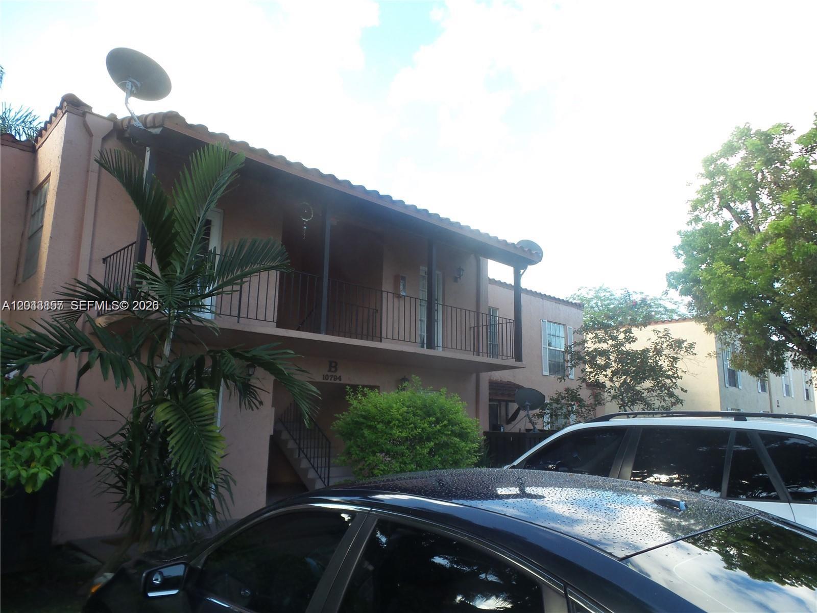 A two-story stucco apartment building features a balcony, a palm tree, and parked cars — 10794 N Kendall Dr # B22, Miami FL 33176, MIAMI, FL