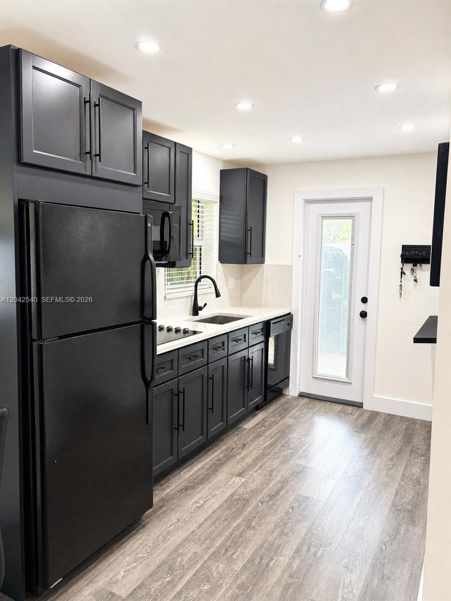 A kitchen features dark cabinets, black appliances, light countertops, and wood-look flooring — 1951 NE 39th St # 138, Lighthouse Point FL 33064, LIGHTHOUSE POINT, FL