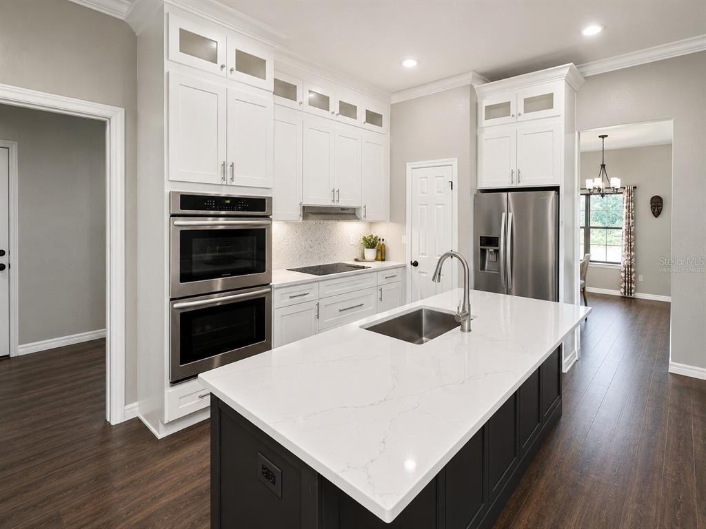A modern kitchen features white upper cabinets, a dark island with a white countertop, and stainless-steel appliances — 14831 SE 1ST PLACE, WILLISTON, FL