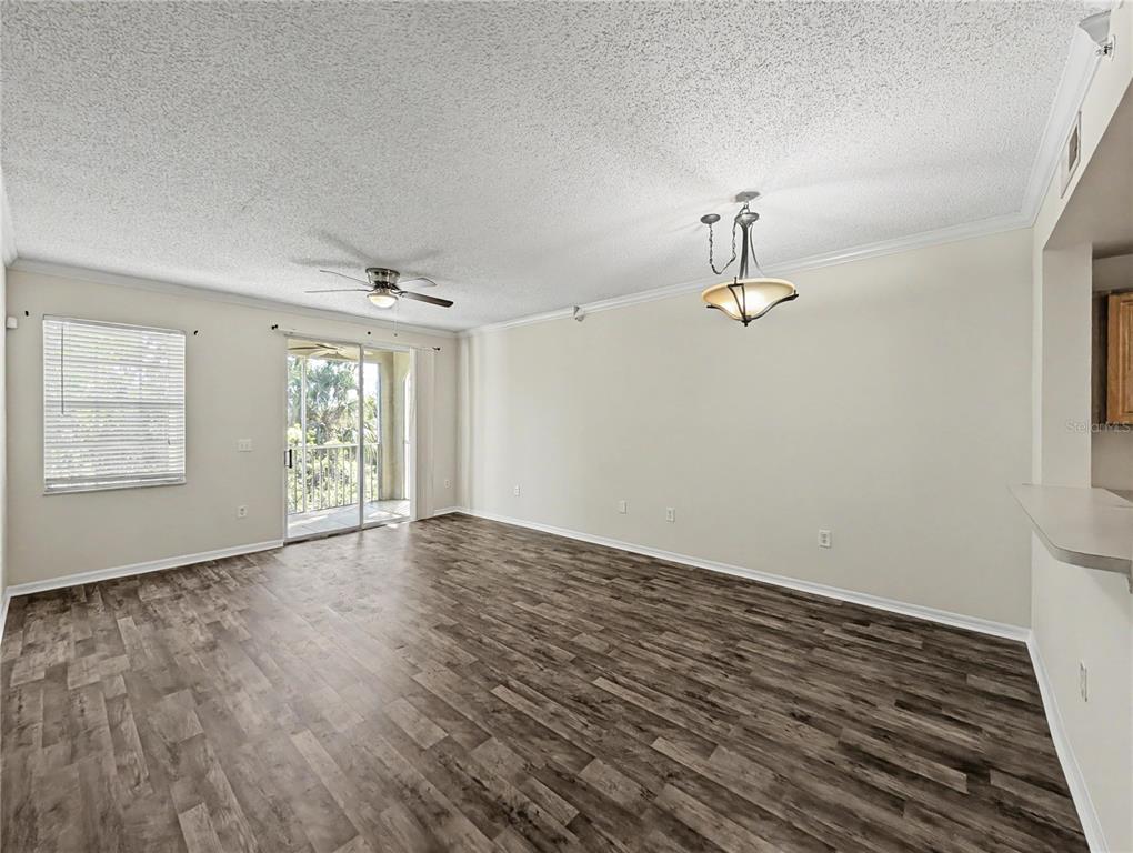 An empty living room features wood-look flooring, a ceiling fan, a chandelier, and a balcony — 5701 BENTGRASS DRIVE UNIT 18-207, SARASOTA, FL