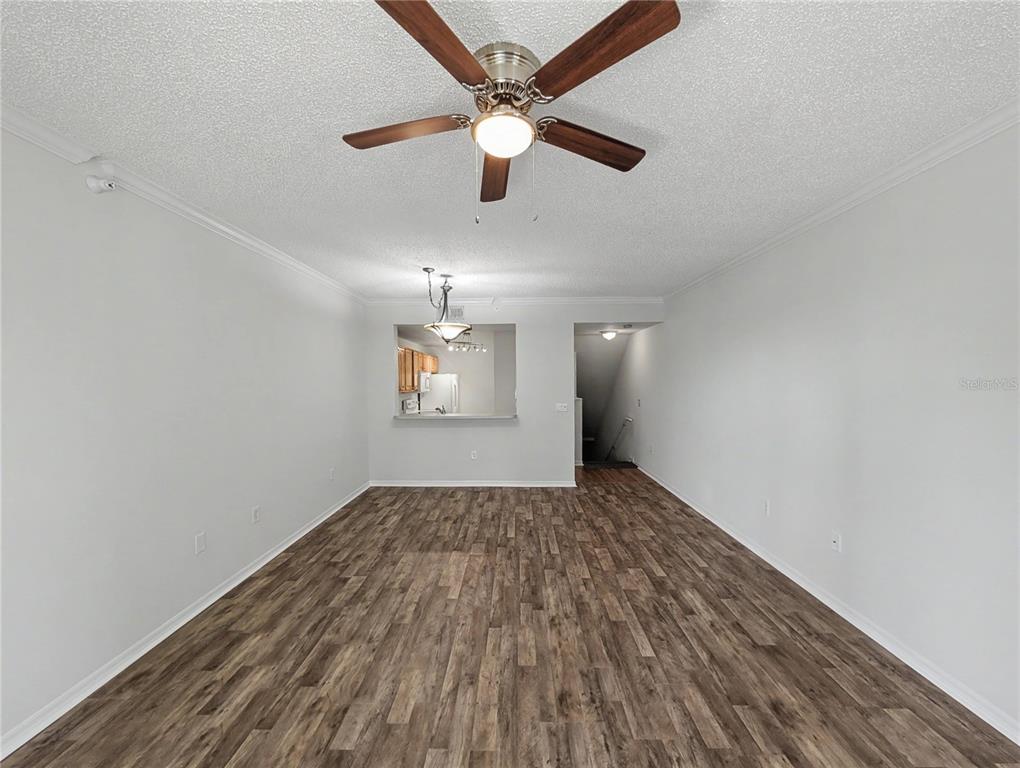 An empty living room features wood-look flooring, a ceiling fan, and a kitchen pass-through window — 5701 BENTGRASS DRIVE UNIT 18-207, SARASOTA, FL