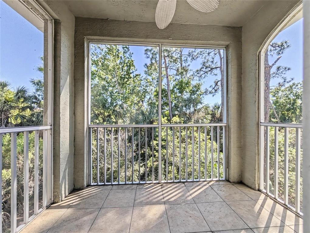 A screened-in balcony with tiled flooring, white railings, and a ceiling fan overlooking trees — 5701 BENTGRASS DRIVE UNIT 18-207, SARASOTA, FL