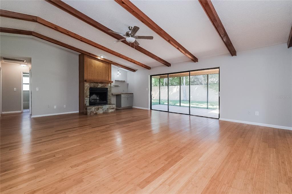A spacious living room features wood-beam vaulted ceilings, hardwood floors, a stone fireplace, and sliding doors — 515 SANDALWOOD DRIVE, PLANT CITY, FL