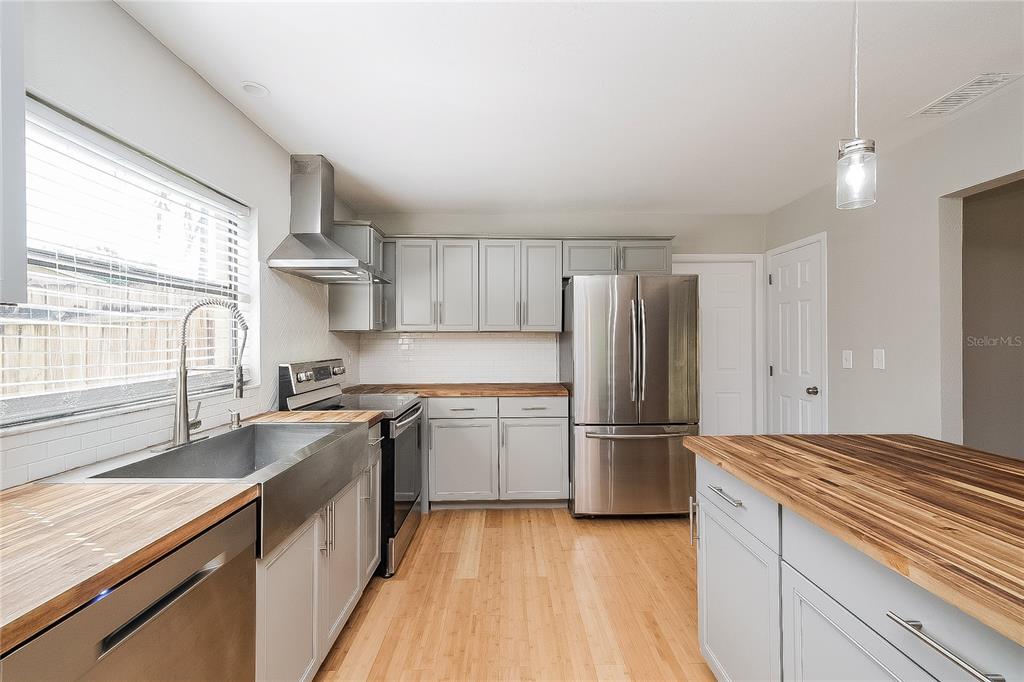 A kitchen features gray cabinets, butcher block countertops, stainless steel appliances, and wood flooring — 515 SANDALWOOD DRIVE, PLANT CITY, FL