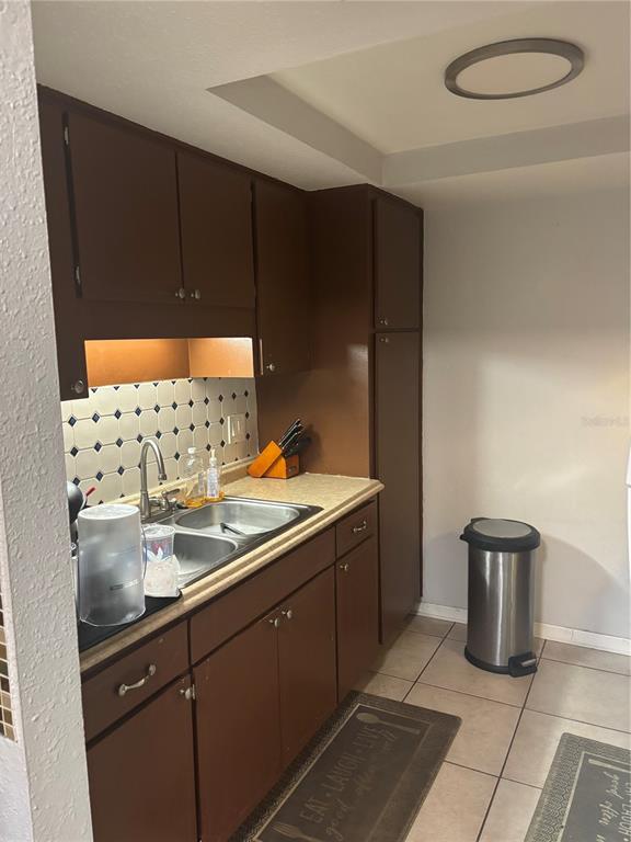 A kitchen features brown cabinets, a double-basin sink, tiled backsplash, and tile flooring — 6080 22ND AVENUE N UNIT 3, ST PETERSBURG, FL