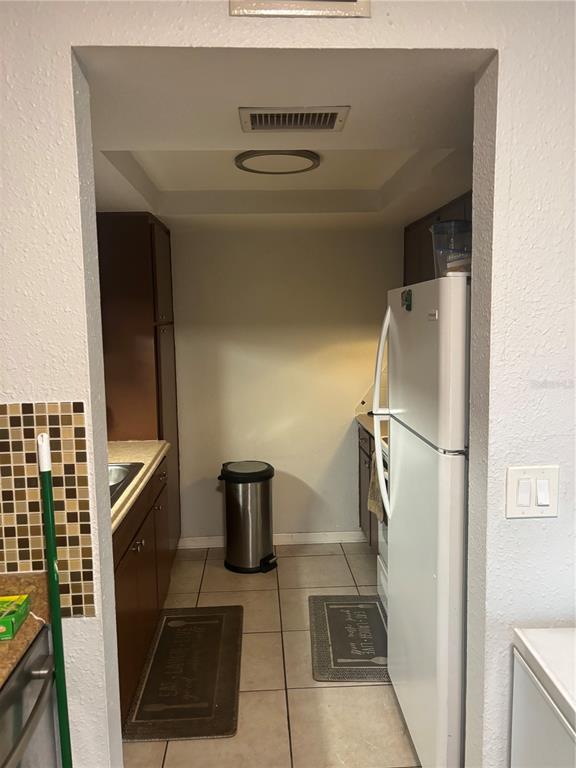 A narrow galley kitchen features brown cabinets, a white refrigerator, and a stainless steel trash can — 6080 22ND AVENUE N UNIT 3, ST PETERSBURG, FL
