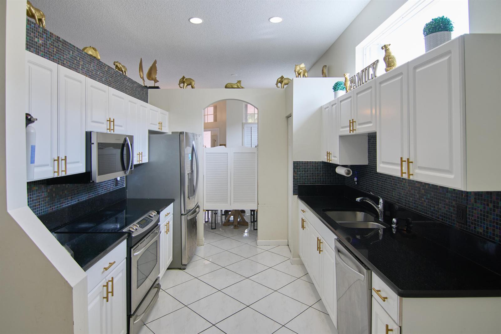 A galley kitchen features white cabinets, black countertops, a mosaic backsplash, and stainless steel appliances — 2824 Waters Edge Circle, FL 33413, FL
