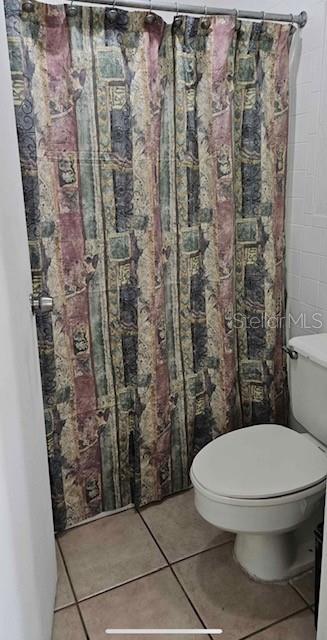 A bathroom features a patterned shower curtain, a white toilet, and light-colored floor tiles — 43420 HIGHWAY 27 UNIT 242, DAVENPORT, FL