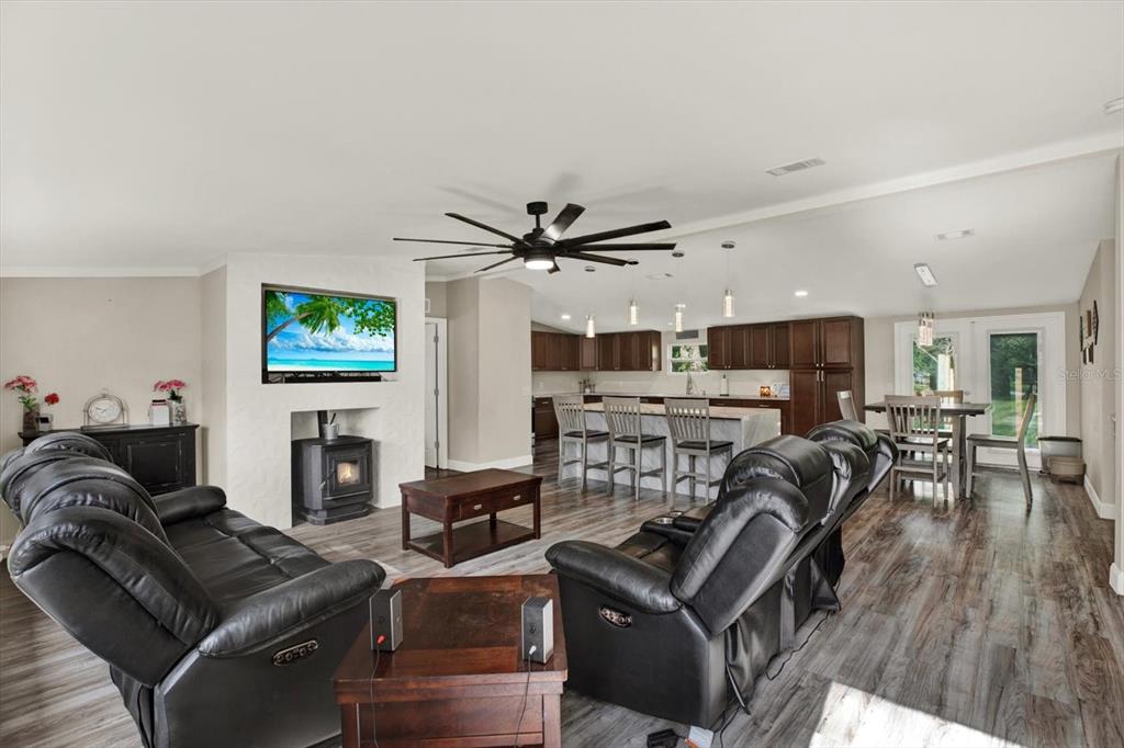 An open-concept living room and kitchen featuring dark leather furniture, wood-look flooring, and a fireplace — 13611 MCINTOSH DRIVE, DADE CITY, FL