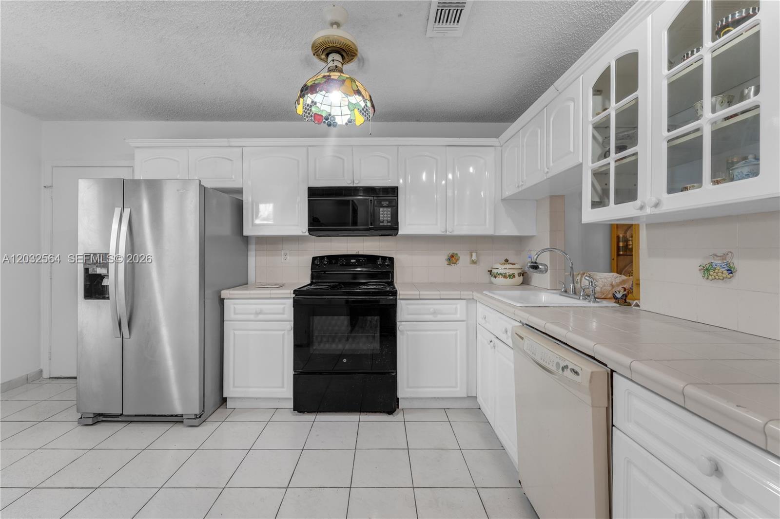 A kitchen features white cabinets, black appliances, a stainless steel refrigerator, and tiled countertops — 13332 SW 113th Ct, Miami FL 33176, MIAMI, FL