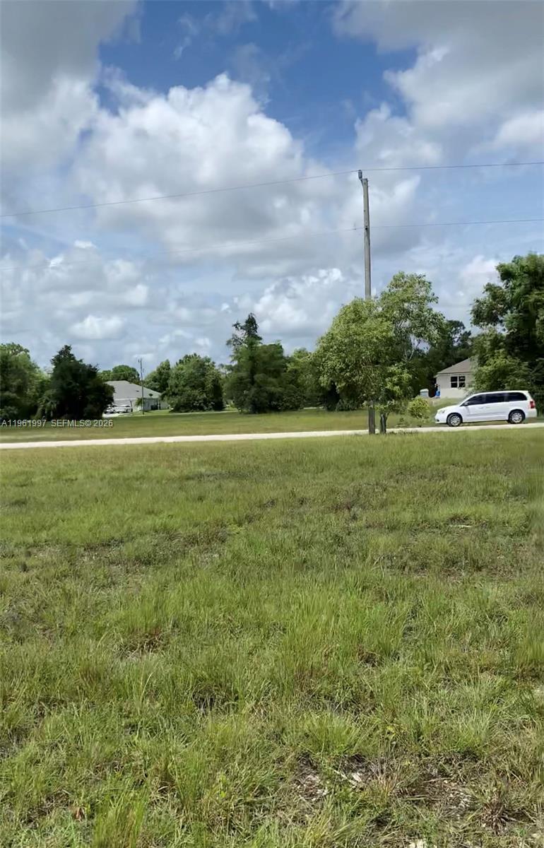 A grassy vacant lot is viewed from the street with trees and houses in the background — 2336 NW 35TH PL, Cape Coral FL 33993, CAPE CORAL, FL