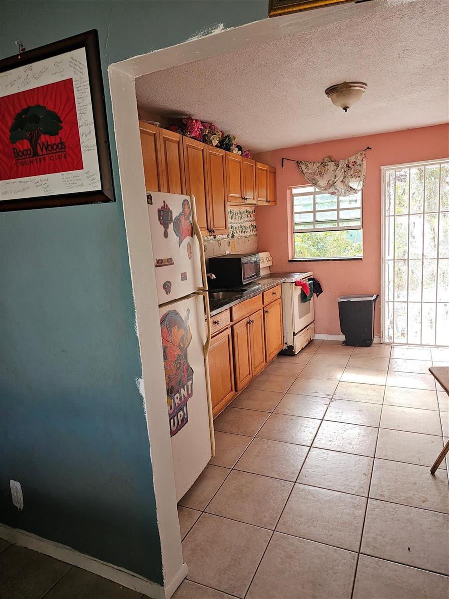 A kitchen with wooden cabinets, tile flooring, a white refrigerator, and a sliding glass door — 2510 NW 6 Street, Pompano Beach FL 33069, POMPANO BEACH, FL