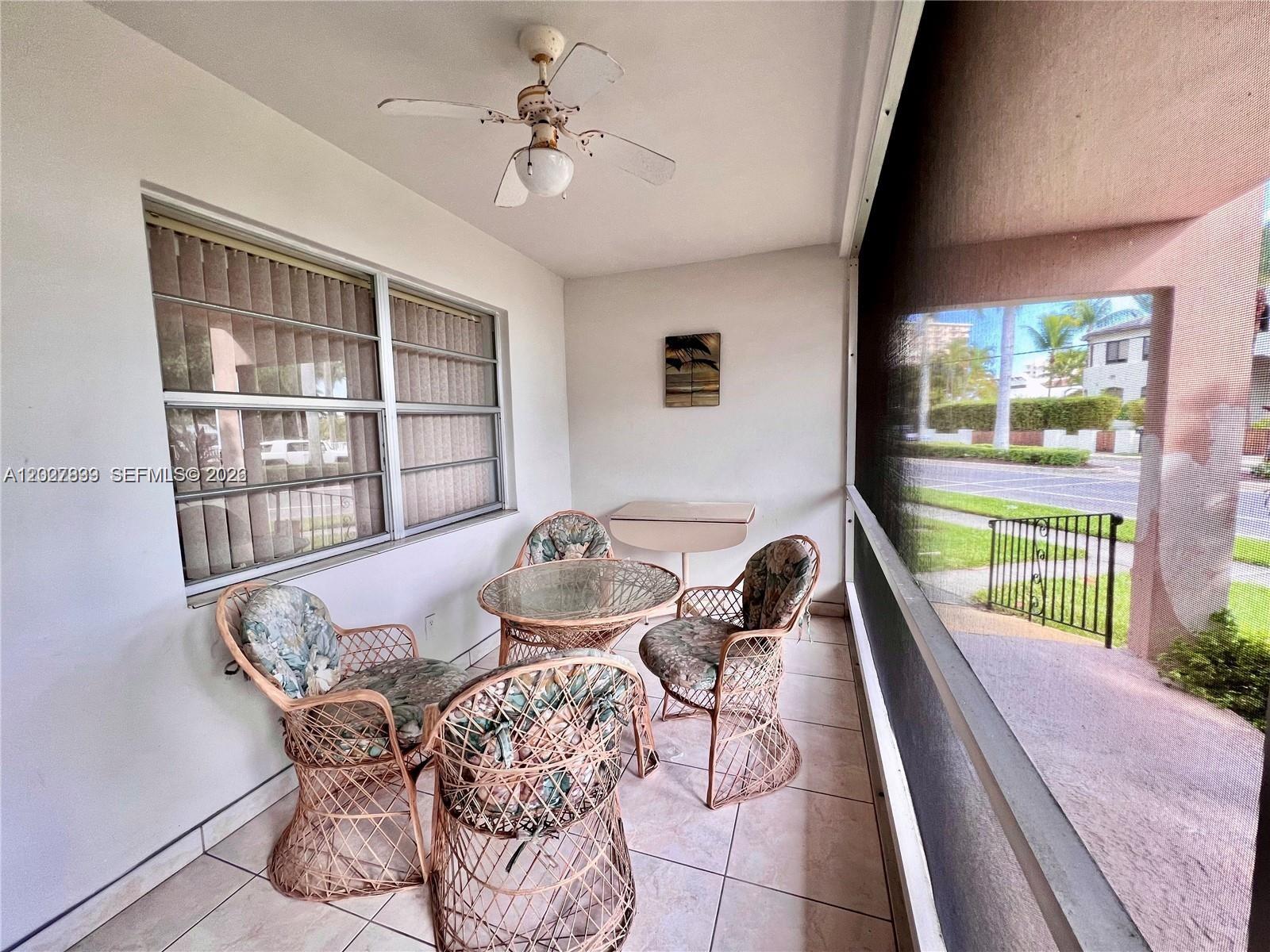 A screened-in patio features tile flooring, a ceiling fan, and a wicker dining set — HALLANDALE BEACH, FL