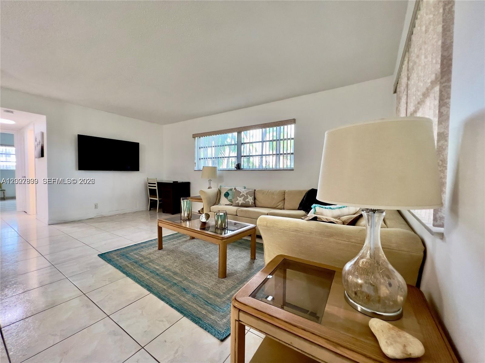 A living room features a beige sectional sofa, a coffee table, and a wall-mounted television — HALLANDALE BEACH, FL