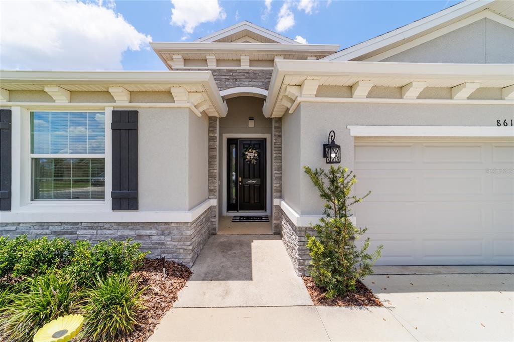 The exterior of a single-story house features a stone facade, a dark front door, and a garage — 8611 SW 49TH CIRCLE, OCALA, FL