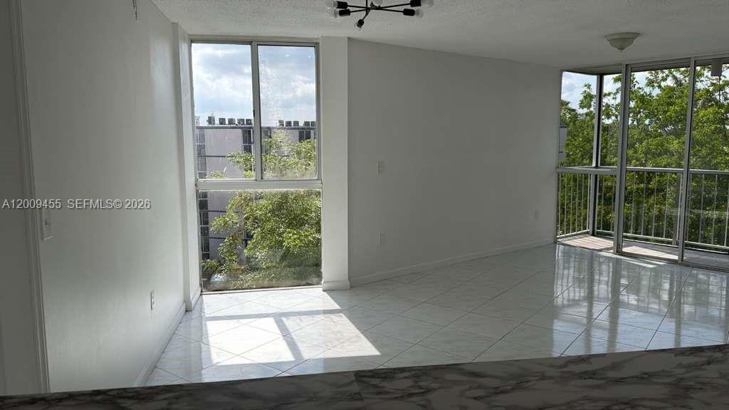 A bright living area features white tile floors, large windows, and a balcony — 6995 NW 186th St # E507, Hialeah FL 33015, HIALEAH, FL
