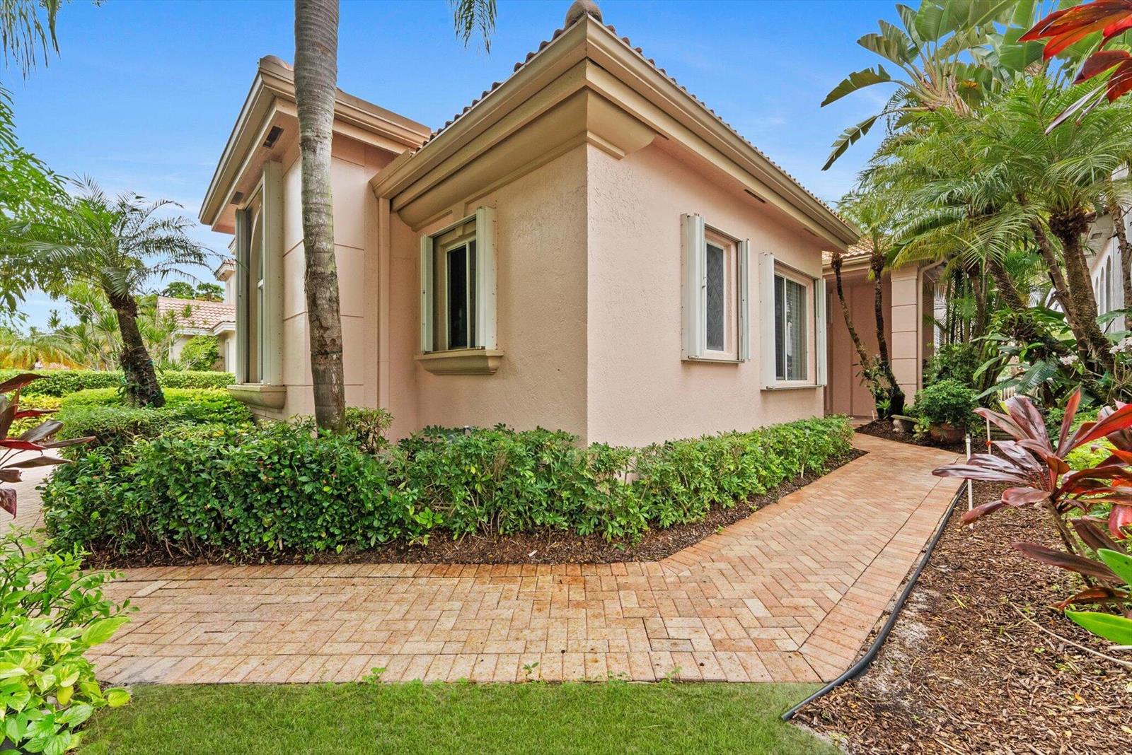 A light pink stucco house exterior features a brick walkway and lush tropical landscaping — 7081 Mallorca Crescent, Boca Raton FL 33433, BOCA RATON, FL