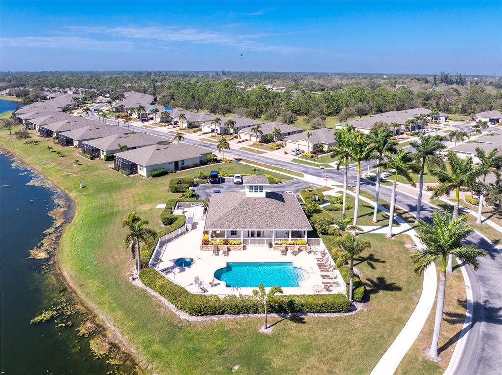 An aerial view shows a community clubhouse with a swimming pool beside a lake — 29633 NIAGARA COURT, ENGLEWOOD, FL