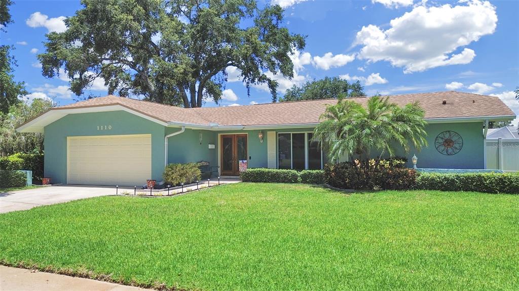 A single-story house with a teal exterior, a two-car garage, and a large front lawn — 1110 MCLEAN STREET, DUNEDIN, FL