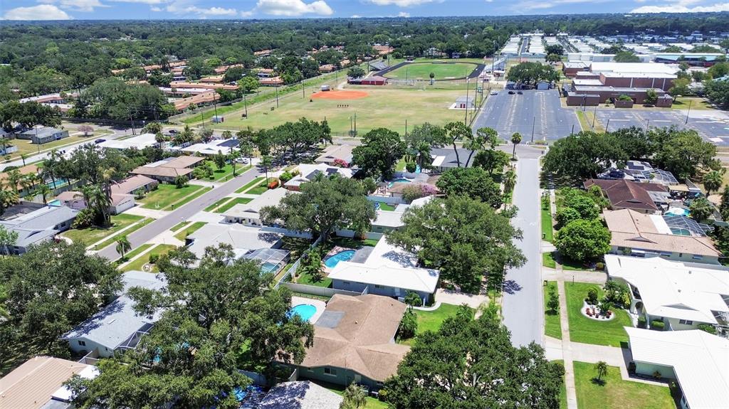An aerial view shows a residential neighborhood with houses, swimming pools, and a nearby school — 1110 MCLEAN STREET, DUNEDIN, FL