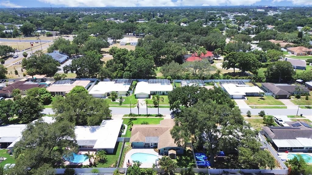 An aerial view shows a suburban neighborhood with single-family homes, swimming pools, and mature trees — 1110 MCLEAN STREET, DUNEDIN, FL