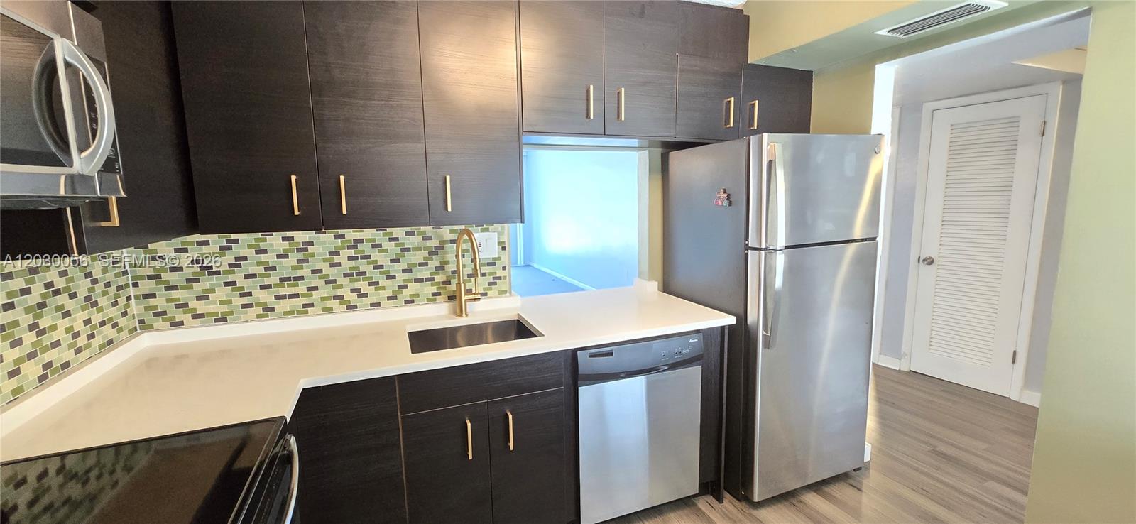 A kitchen features dark wood cabinets, stainless steel appliances, white countertops, and a green backsplash — 1201 NE 191st St # G306, Miami FL 33179, MIAMI, FL