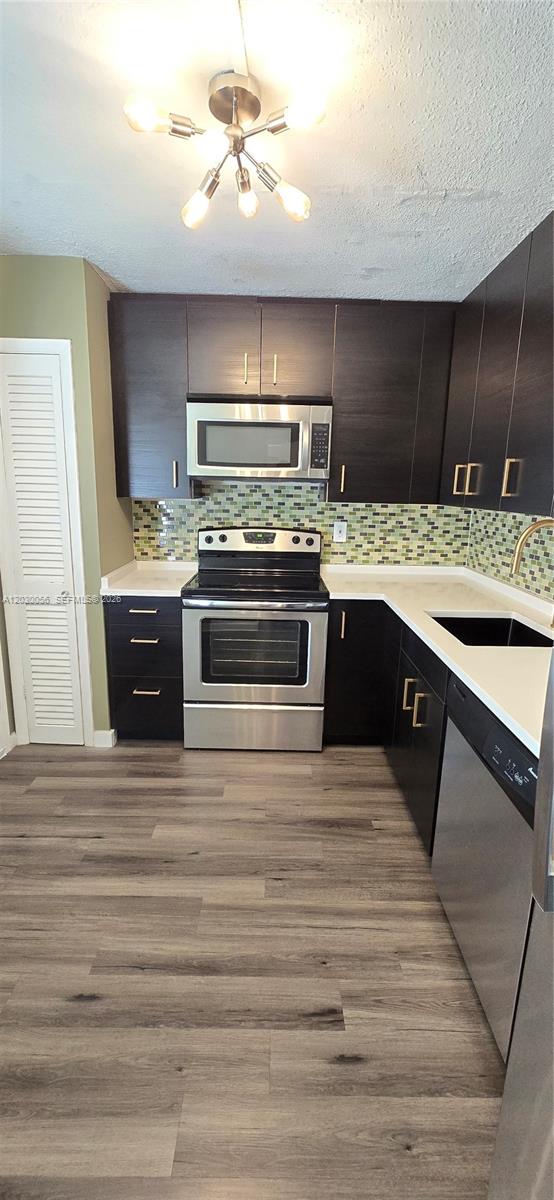 A kitchen features dark wood cabinets, stainless steel appliances, and a green mosaic tile backsplash — 1201 NE 191st St # G306, Miami FL 33179, MIAMI, FL