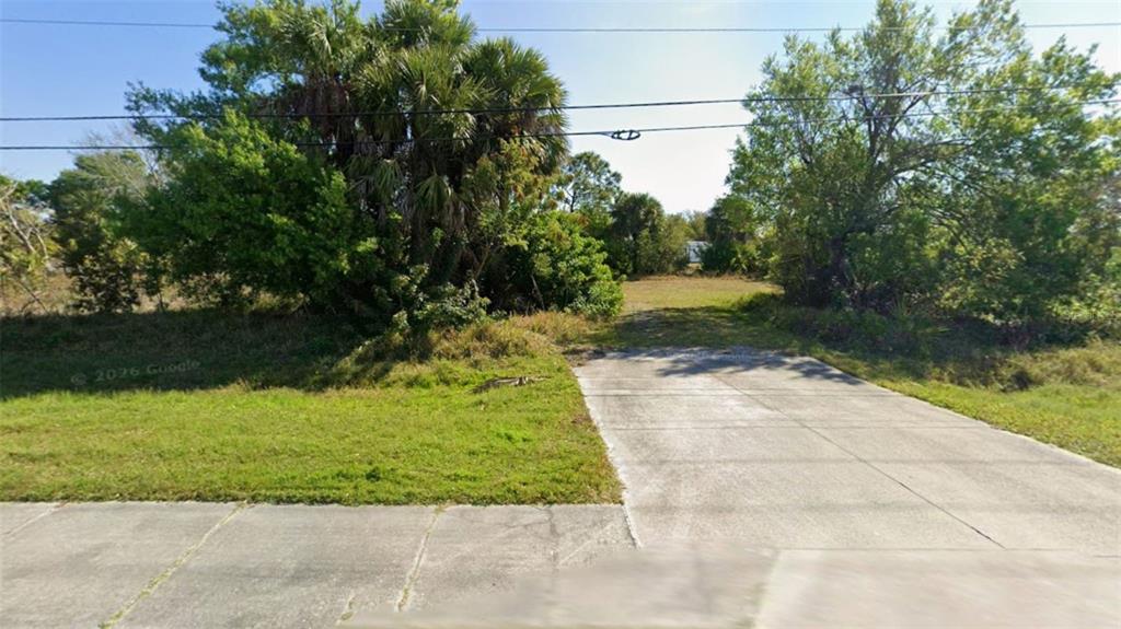 A concrete driveway leads to a vacant, grassy lot surrounded by trees and vegetation — 1828 COOPER STREET, PUNTA GORDA, FL