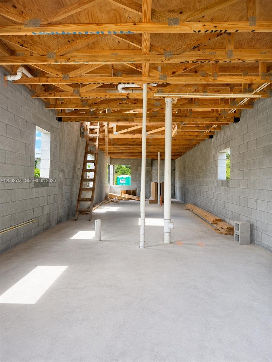 An unfinished interior space features concrete block walls, exposed wooden trusses, and vertical plumbing pipes — 3165 NW 61st St, Miami FL 33142, MIAMI, FL