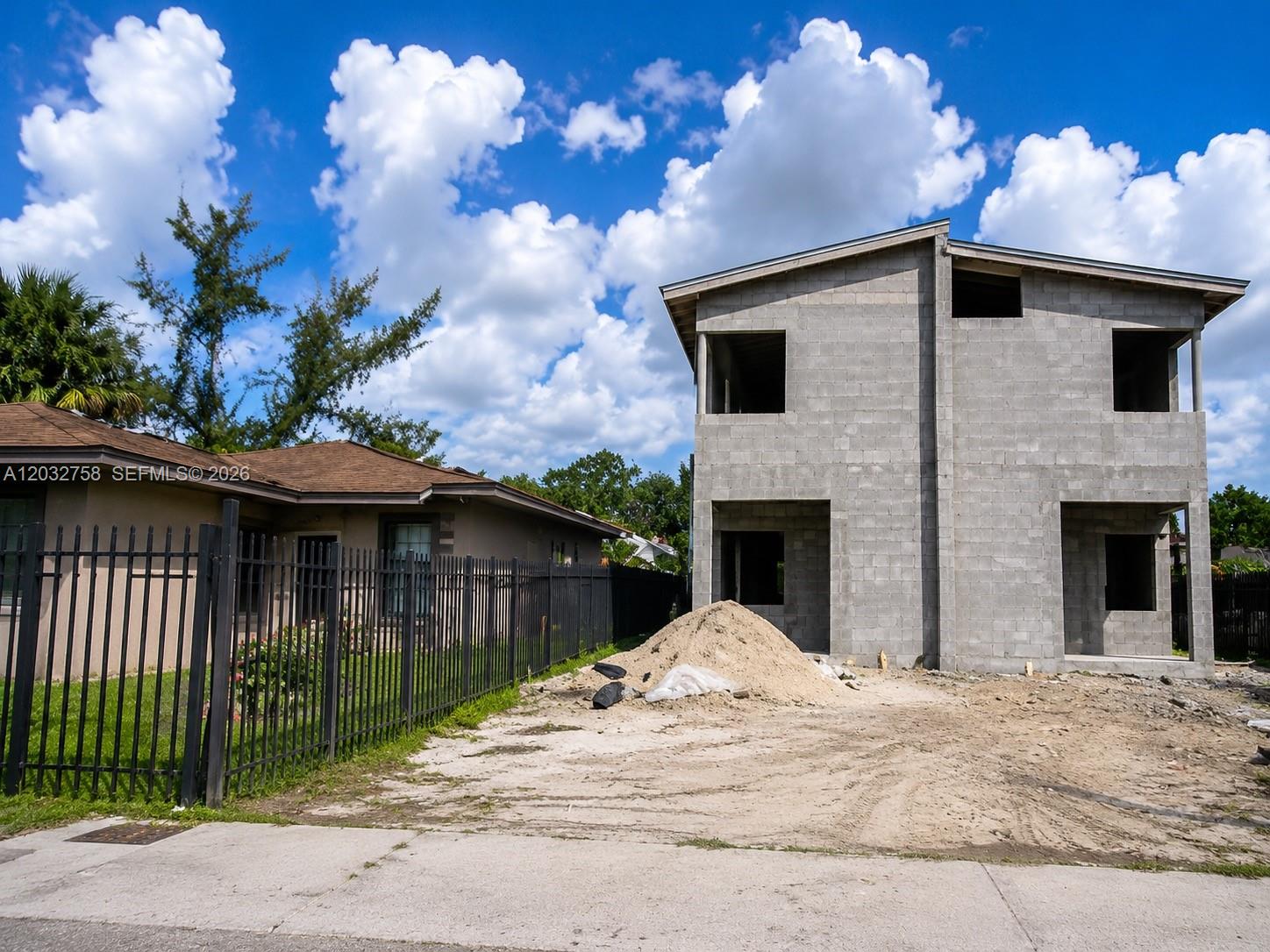 A two-story concrete block house under construction stands next to an existing single-story home — 3165 NW 61st St, Miami FL 33142, MIAMI, FL