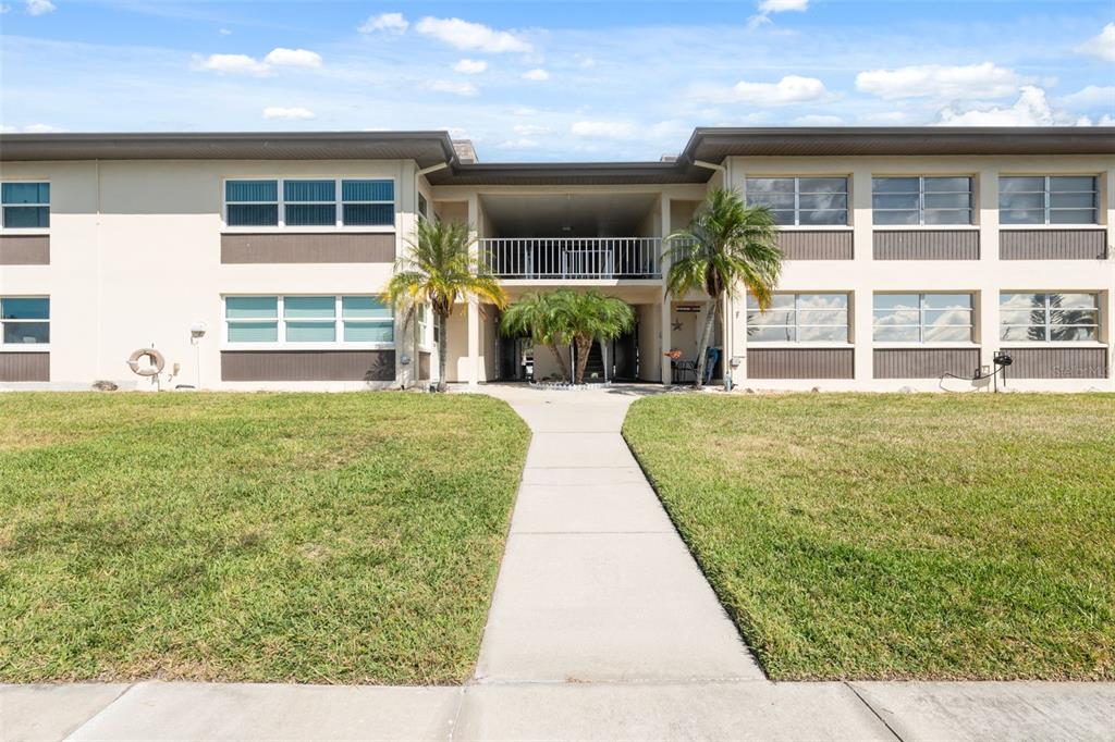 A two-story apartment building with a central walkway, palm trees, and a grassy lawn — 4812 JASPER DRIVE UNIT 105, NEW PORT RICHEY, FL