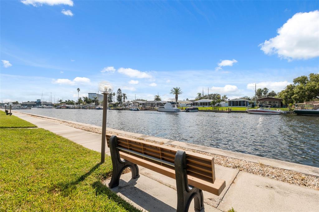 A park bench sits on a concrete walkway overlooking a canal with docked boats — 4812 JASPER DRIVE UNIT 105, NEW PORT RICHEY, FL