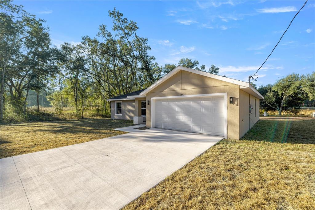 A single-story house with a white garage door and a concrete driveway sits on grass — 11380 SE 123RD AVENUE, DUNNELLON, FL