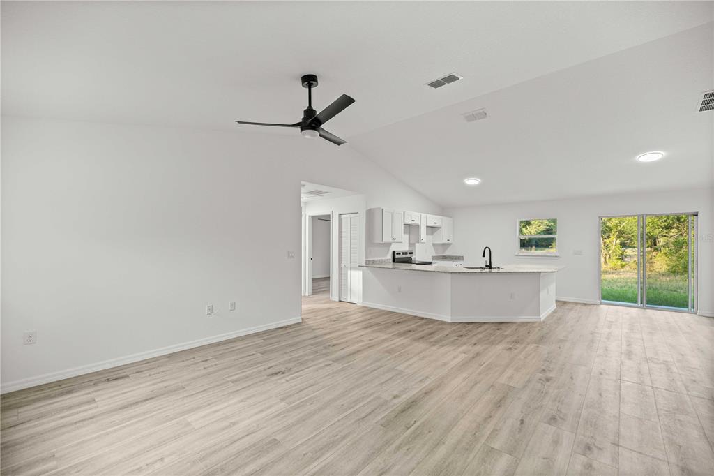 An open-concept living area with light wood-look flooring, a vaulted ceiling, and a kitchen island — 11380 SE 123RD AVENUE, DUNNELLON, FL