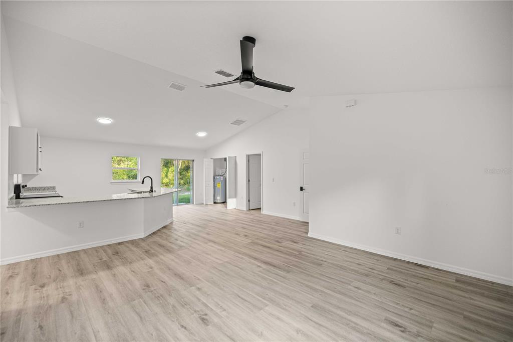 An open-concept living area features light wood-look flooring, white walls, and a kitchen peninsula — 11380 SE 123RD AVENUE, DUNNELLON, FL