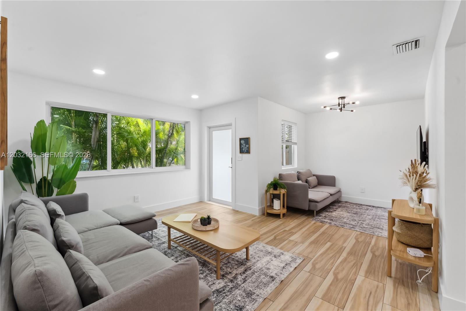 A bright living room features light wood-look tile flooring, gray sofas, and large windows — 1480 NE 117th St # 1480, Miami FL 33161, MIAMI, FL