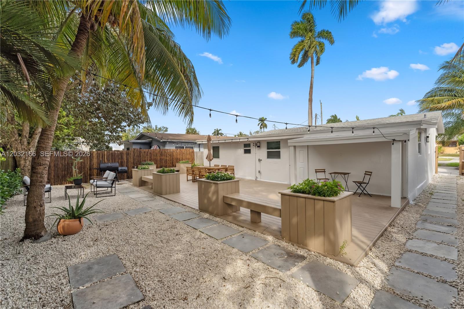 A backyard features a wooden deck with built-in planters, gravel ground, and string lights — 1480 NE 117th St # 1480, Miami FL 33161, MIAMI, FL