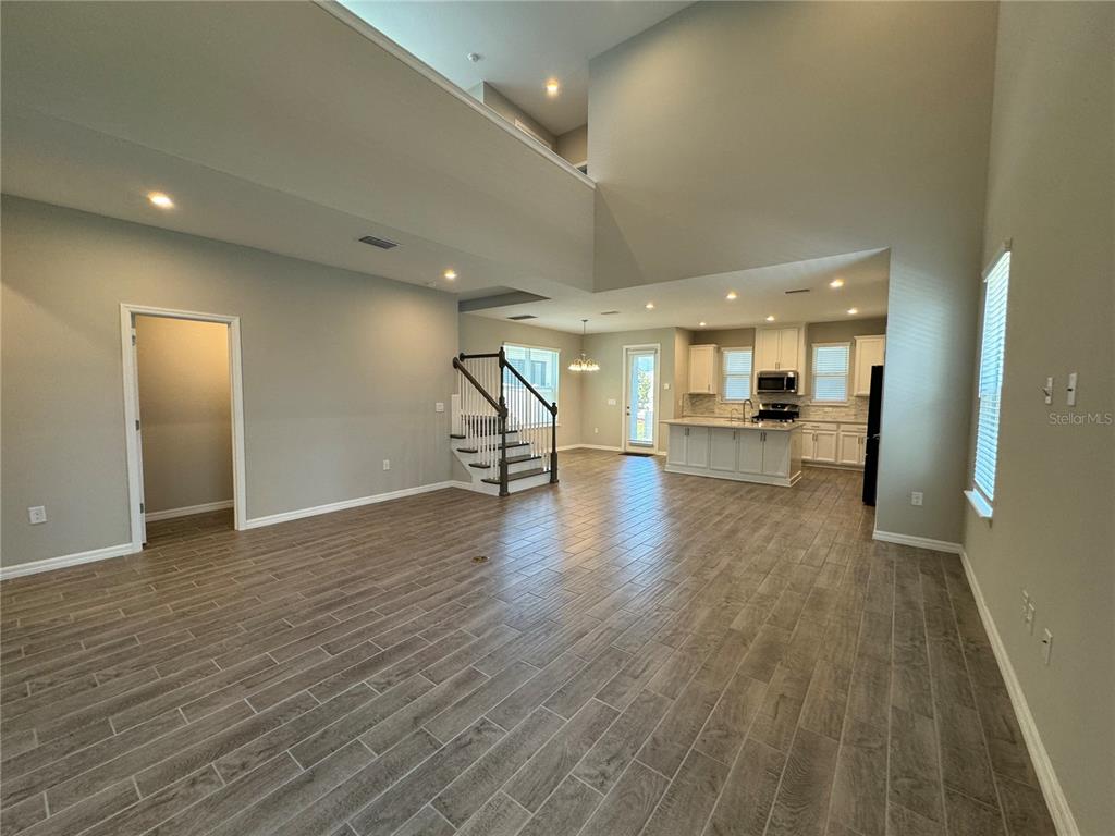 An open-concept living area features wood-look tile flooring, a staircase, and a kitchen with white cabinets — 13823 RANGELAND BOULEVARD, ODESSA, FL