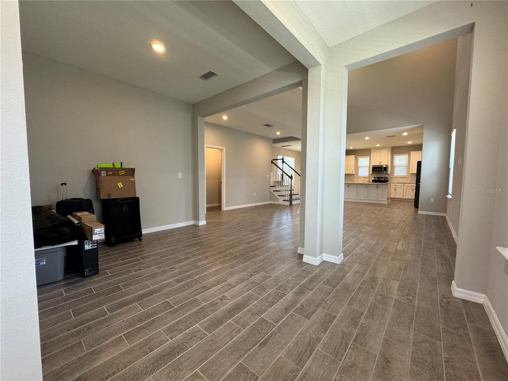 An open-concept living area with tile flooring leads to a kitchen and a staircase — 13823 RANGELAND BOULEVARD, ODESSA, FL