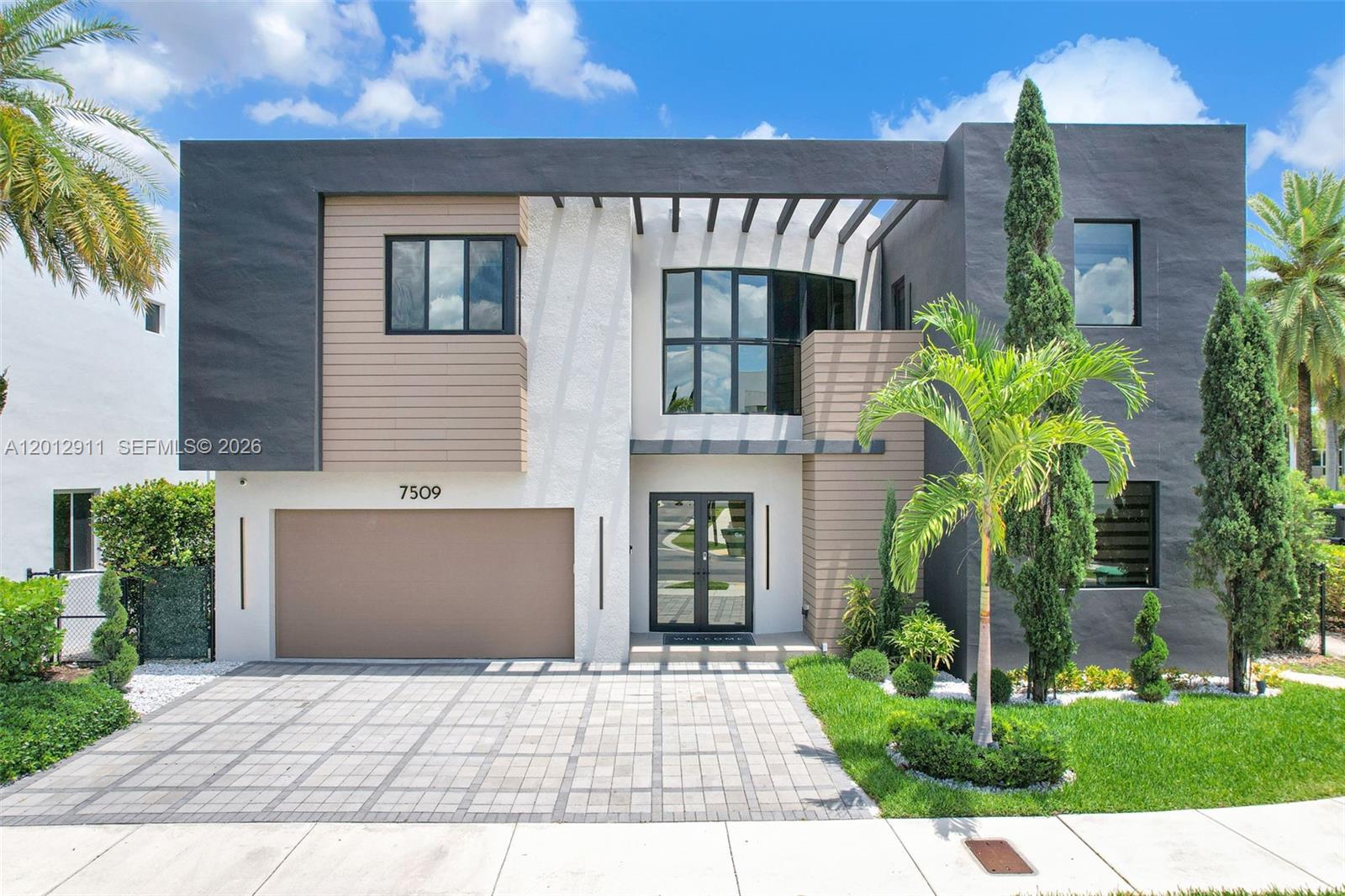 A modern two-story house features a gray and white facade with wood-look siding and a pergola — 7509 NW 99th Ave, Doral FL 33178, DORAL, FL