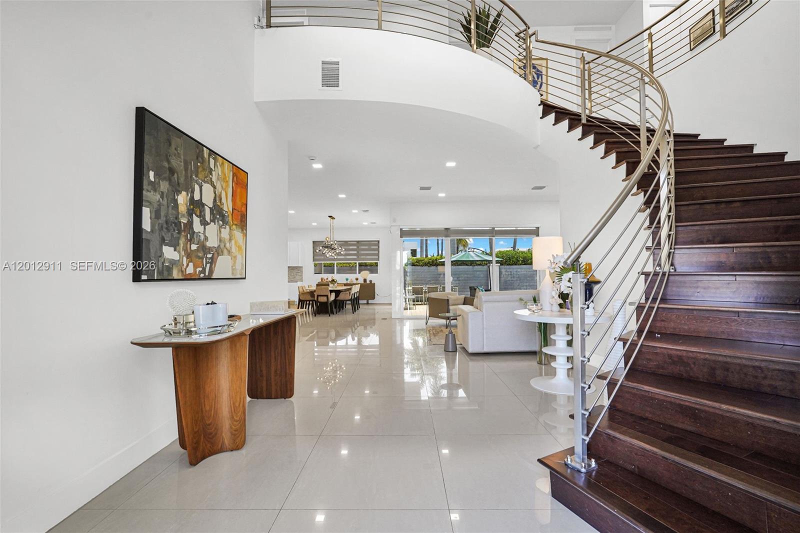 A bright, open-concept living area features a curved wooden staircase and polished tile flooring — 7509 NW 99th Ave, Doral FL 33178, DORAL, FL