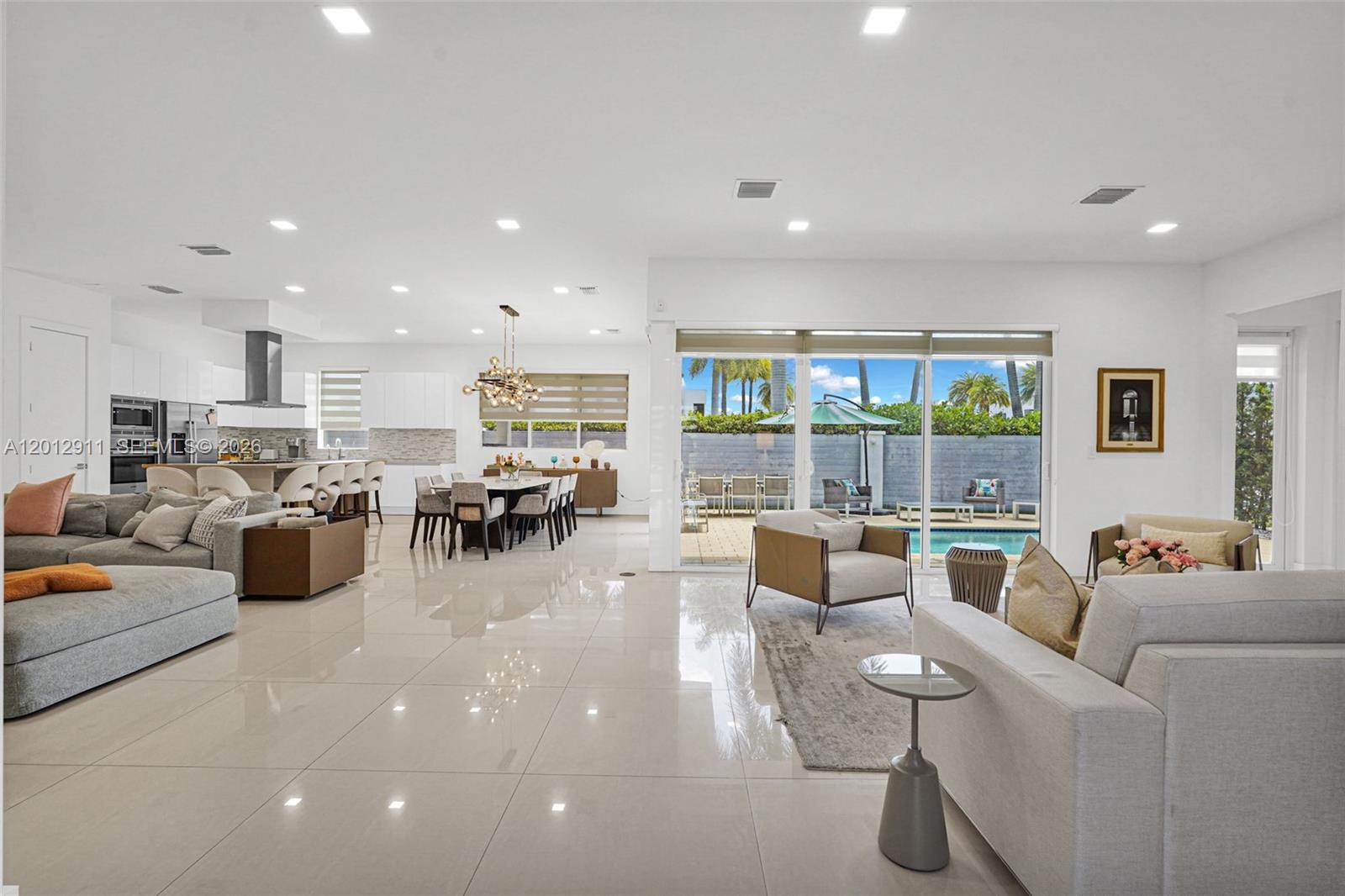 A bright, open-concept living and dining area features white tile floors and a backyard pool — 7509 NW 99th Ave, Doral FL 33178, DORAL, FL