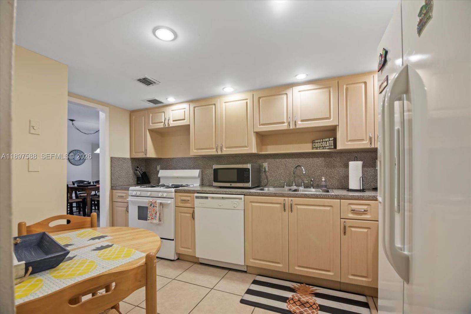 A kitchen features light wood cabinets, white appliances, a tiled backsplash, and a dining table — 3140 S Ocean Dr # 207, Hallandale Beach FL 33009, HALLANDALE BEACH, FL