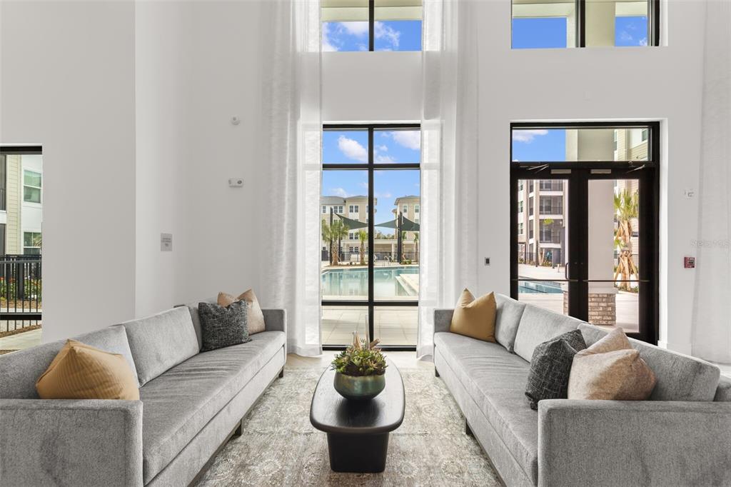 A bright, high-ceilinged lounge features two gray sofas facing a central coffee table and pool — 7210 INTERBAY BOULEVARD UNIT B1, TAMPA, FL